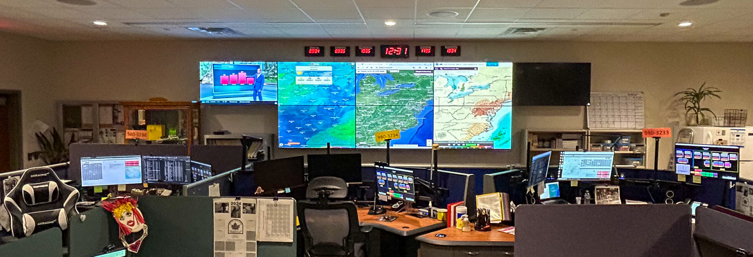An office with three desks facing a tv wall showing maps