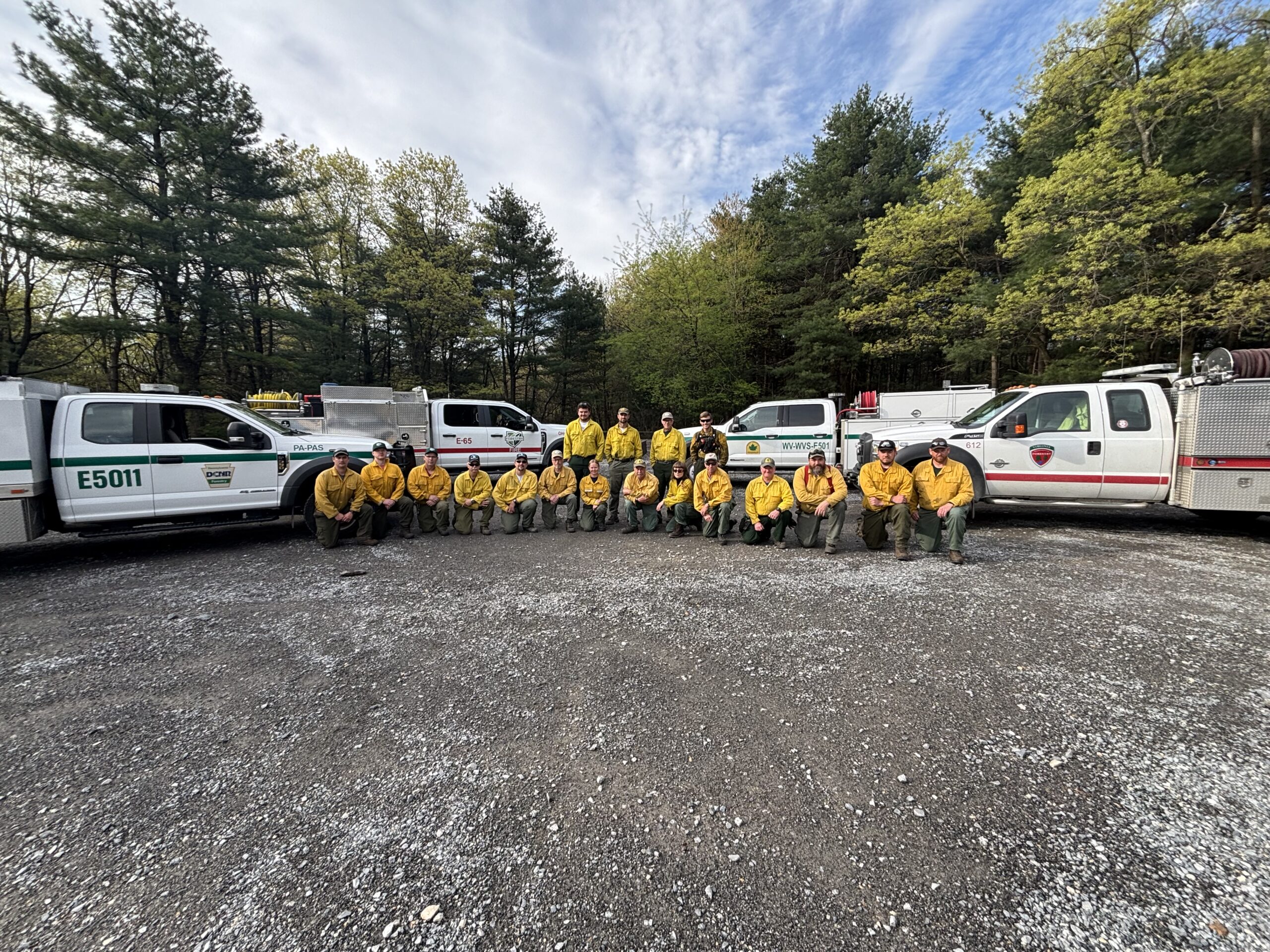 Wildland firefighters in yellow and green grouped with fire engines in background.
