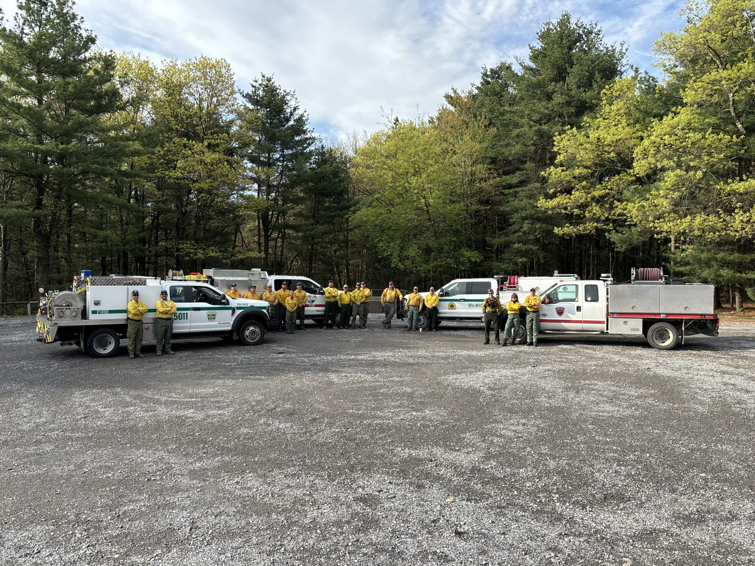 Wildland firefighters in green and yellow standing next to four fire engines.